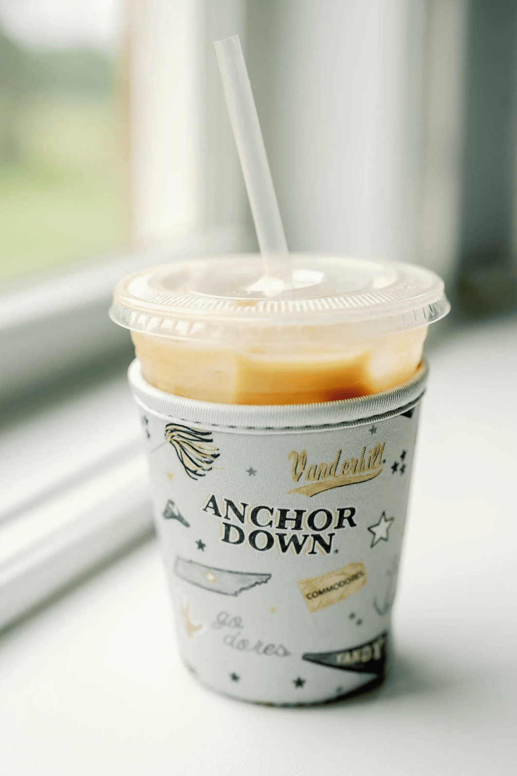 18 Nashville FINDS for Late Summer: Jewelry, Decor & More - 10 A plastic cup with an iced drink and straw sits in a Vanderbilt-branded sleeve that reads "Anchor Down," placed on a white windowsill—capturing the essence of late summer and FINDS Nashville.