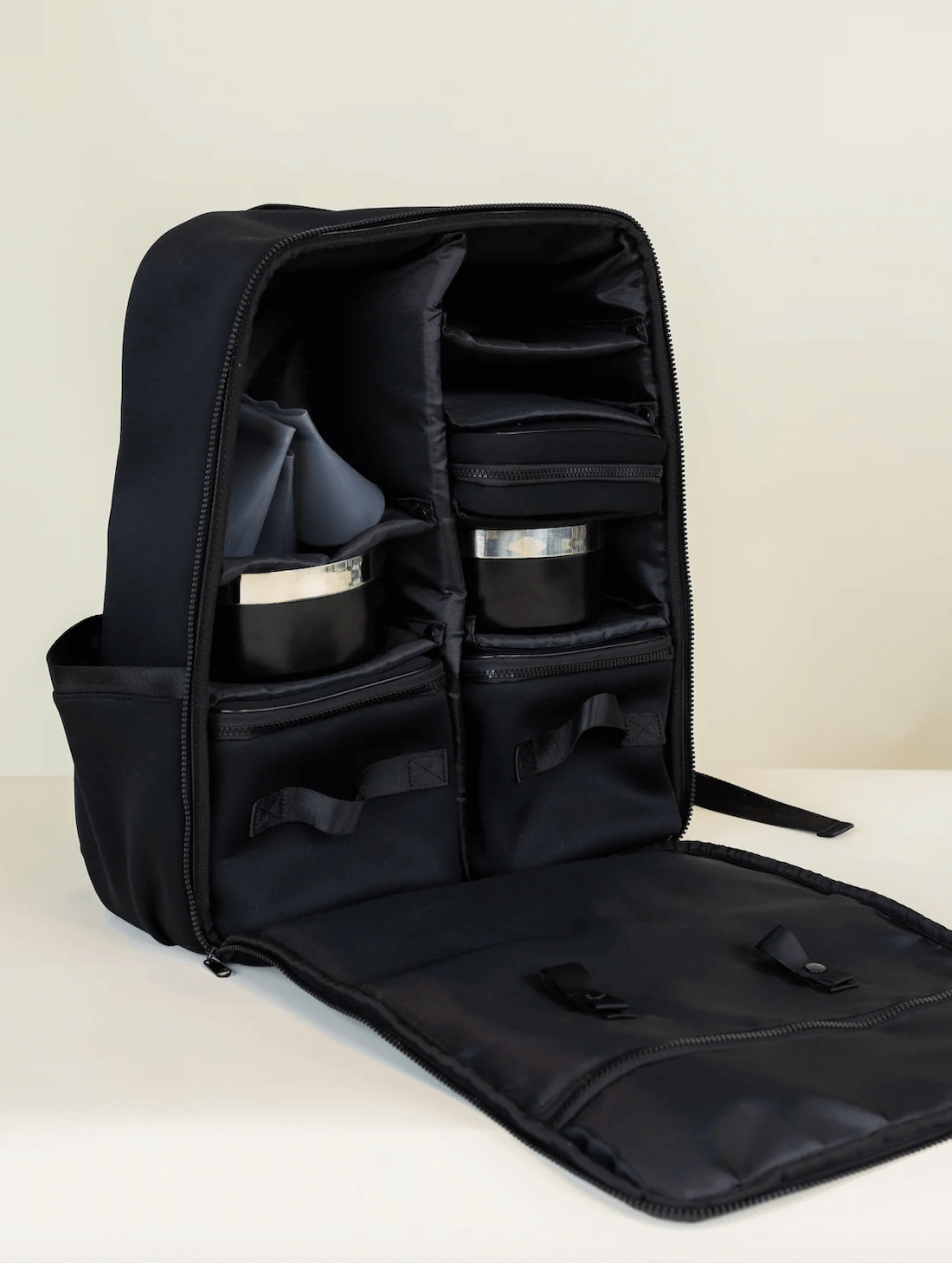 18 Nashville FINDS for Late Summer: Jewelry, Decor & More - 8 A black backpack from FINDS Nashville with its front panel unzipped, revealing multiple compartments and two round containers inside—perfect for staying organized during late summer adventures.