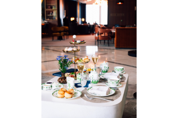 A table set for Afternoon Tea features tiered trays of pastries, teacups, scones, and champagne in a modern lounge—an elegant setting reminiscent of Downton Abbey sophistication.
