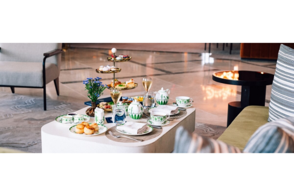 A table set for Downton Abbey Tea features fine china, pastries, sandwiches, desserts on a tiered tray, and two glasses of champagne in a modern lounge setting.