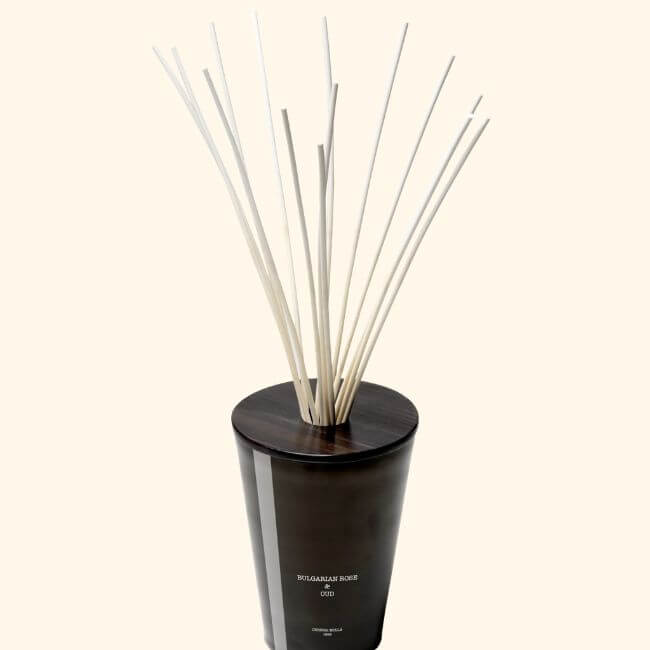 18 Nashville Luxe Loves: Statement Jewelry, Custom Hats & Summer Showstoppers - 17 A dark glass diffuser bottle with a wooden cap, containing several tall, thin reed sticks arranged upright, for adding sophisticated fragrance to any space.
