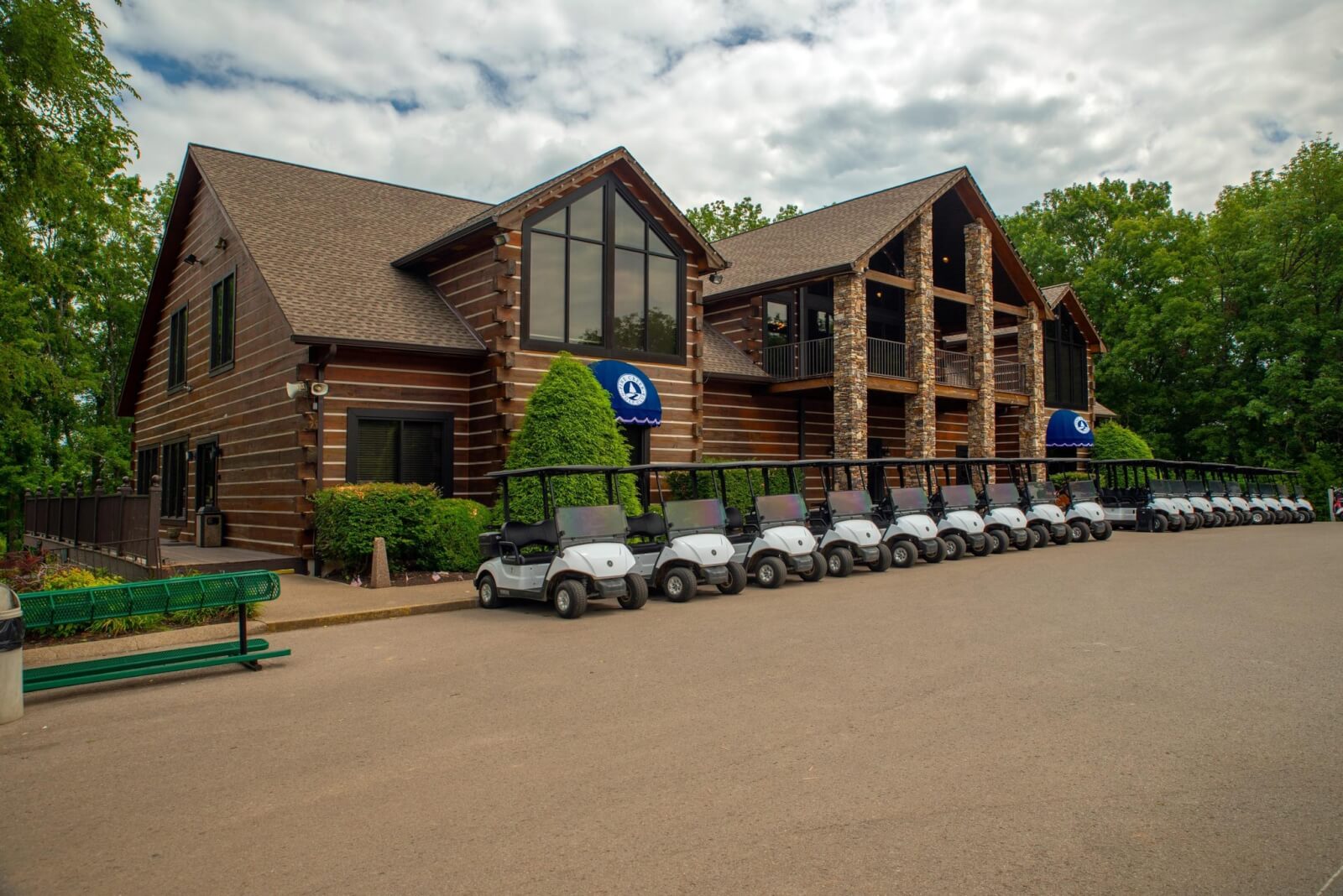 A row of golf carts parked in front of a large log cabin-style building surrounded by trees under a partly cloudy sky, evoking the inviting atmosphere found at many Nashville golf courses.