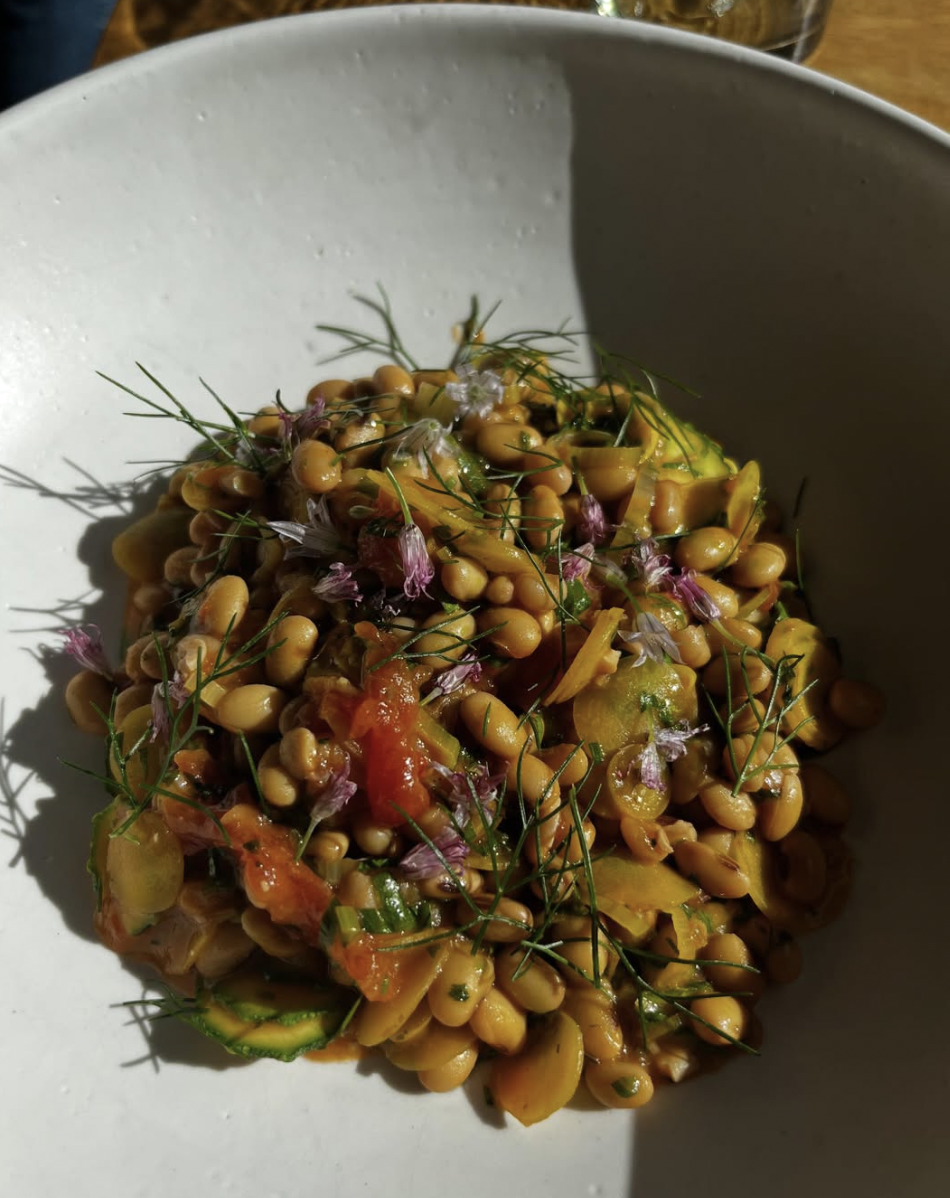 A white bowl filled with a salad of white beans, diced tomatoes, herbs, and garnished with small purple flowers and dill—perfect for those seeking upscale plant-based meals inspired by Nashville’s vibrant vegan restaurants.