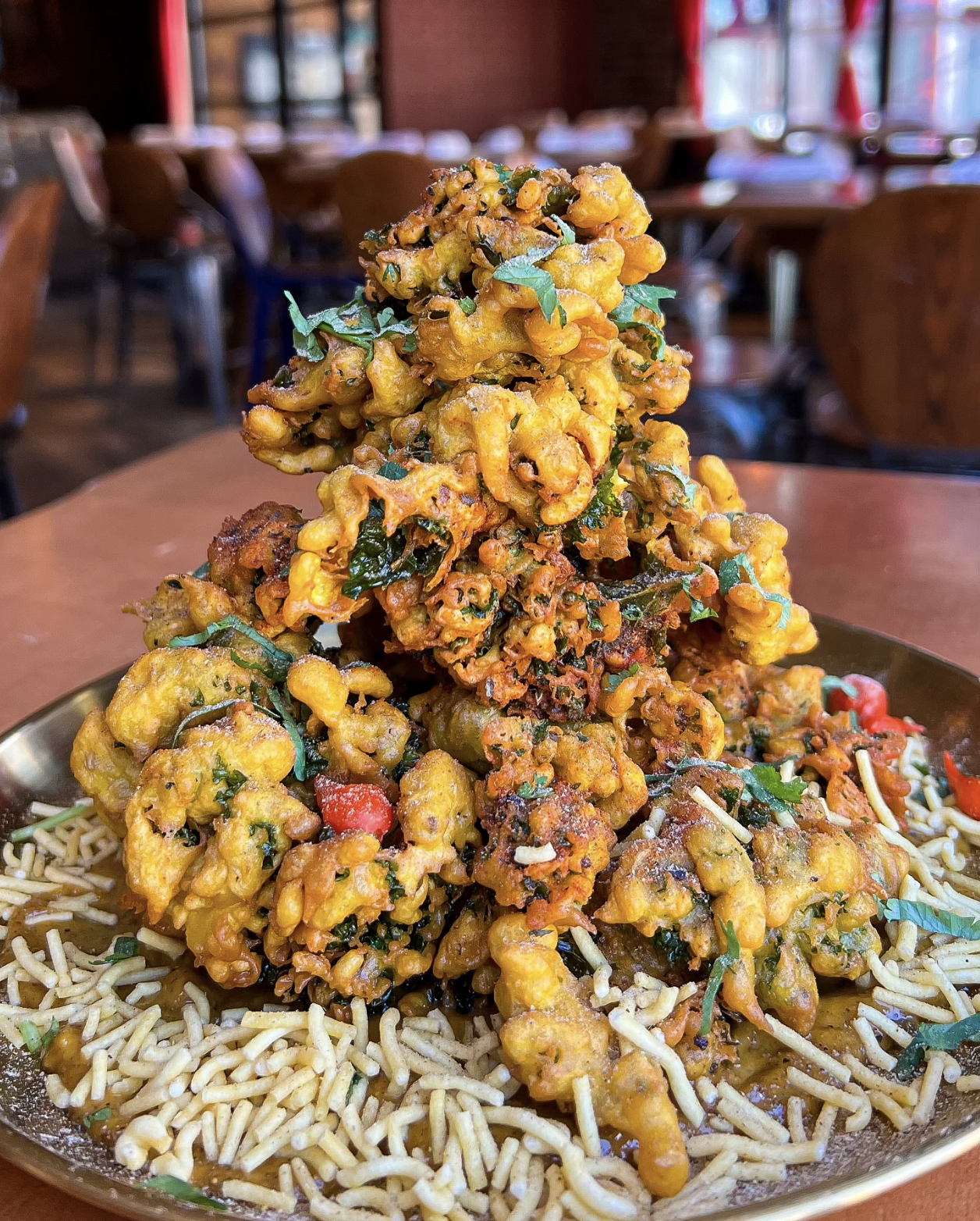 A pile of vegetable pakoras garnished with herbs is served on a plate over a layer of sev, capturing the essence of upscale plant-based meals in a stylish Nashville vegan restaurant setting.