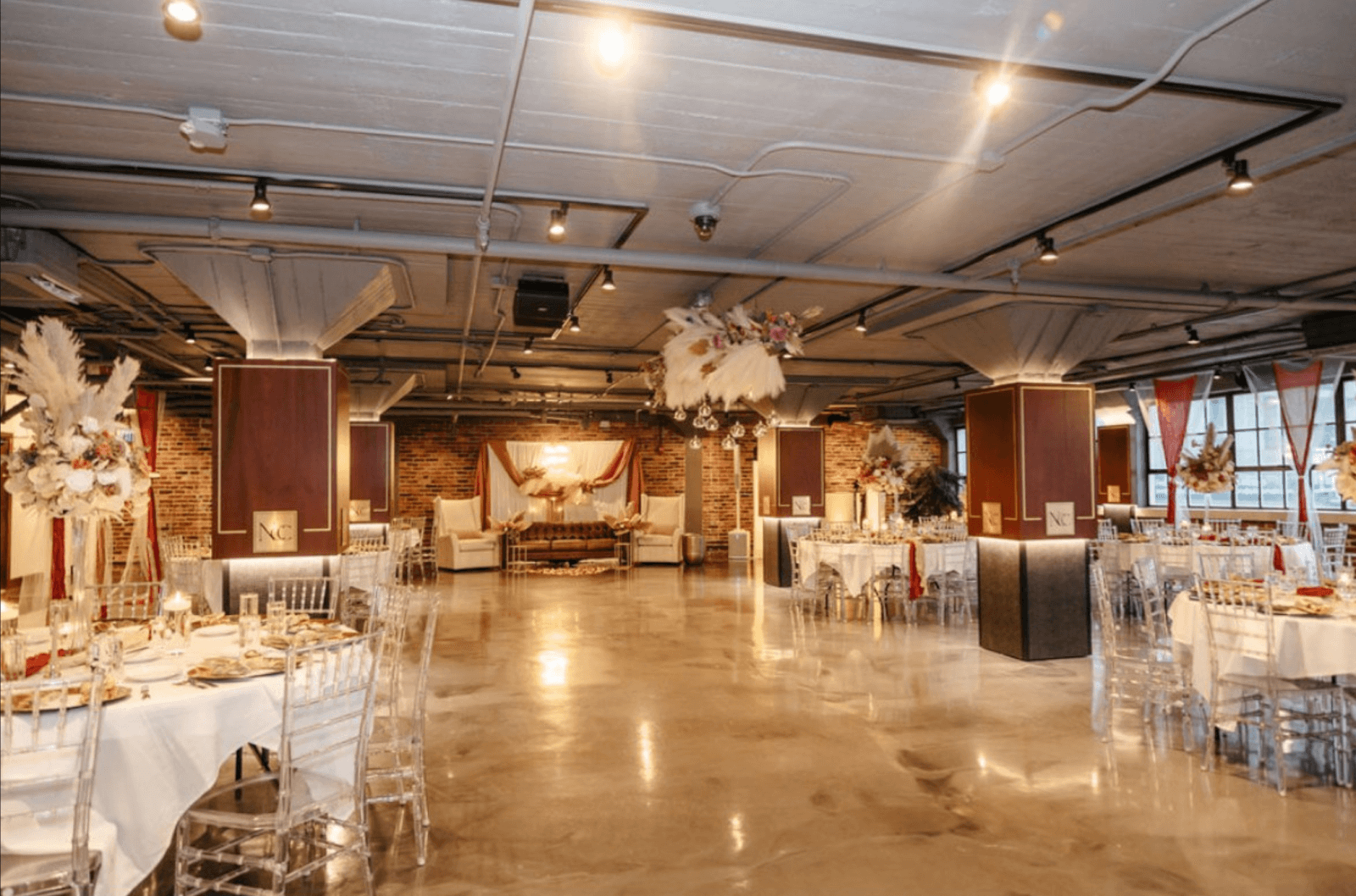 Spacious event venue with polished concrete floors, exposed brick walls, elegant floral decorations, clear chairs, and tables set for a formal gathering—perfect for Nashville Deals and August 2025 celebrations.