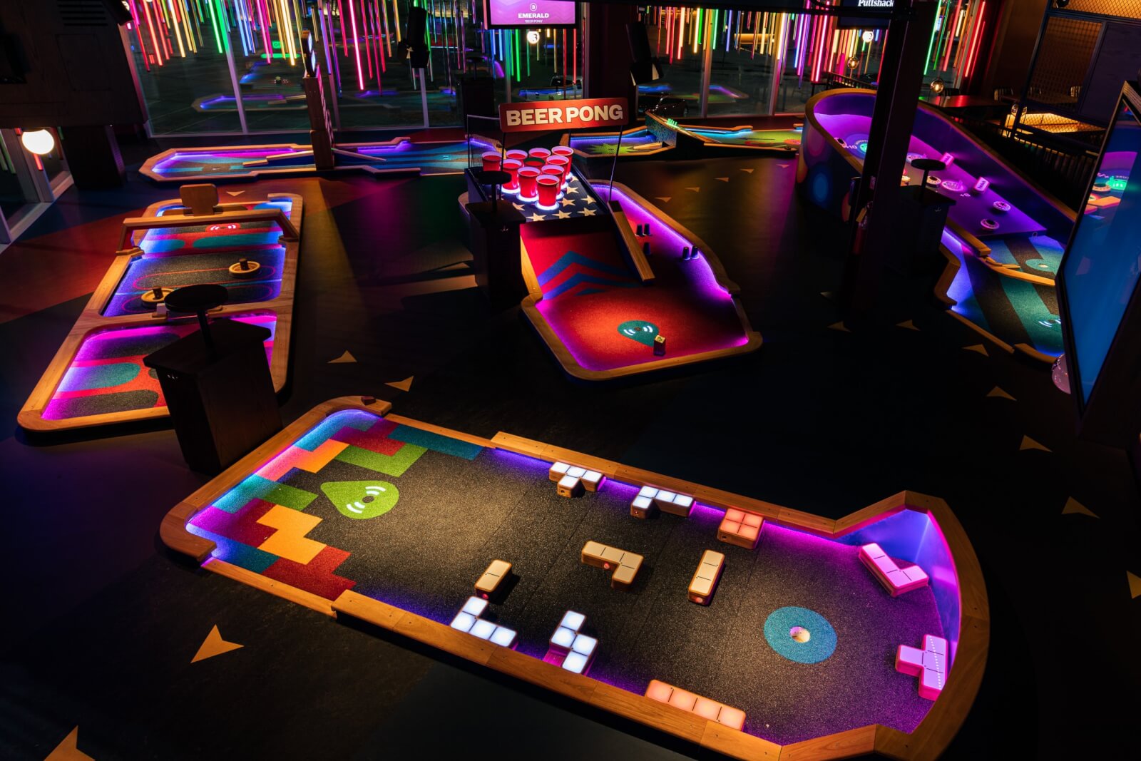 A brightly lit indoor mini golf course with colorful neon lights and themed holes—including a beer pong-themed hole in the center—offers unforgettable fun and exciting Nashville Steals perfect for your August 2025 adventure.
