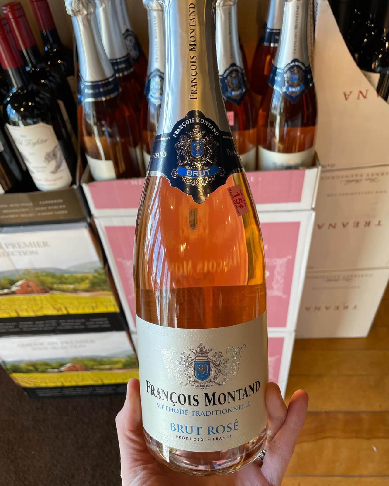 A hand holds a bottle of François Montand Brut Rosé sparkling wine in front of a display of similar bottles—one of the perfect summer wines to sip for a refreshing treat.