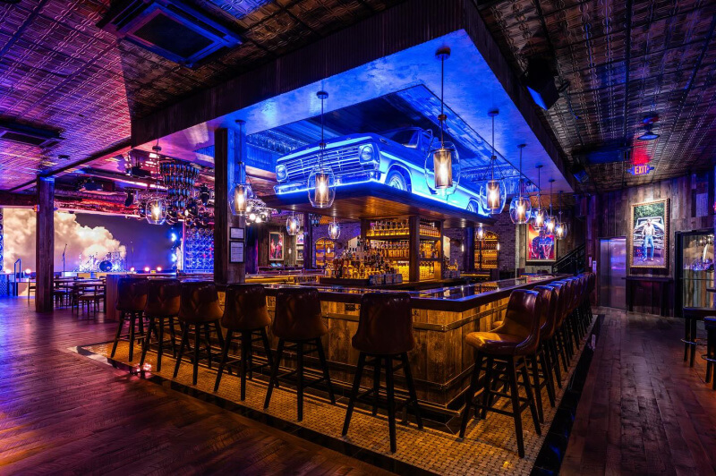 A bar with high stools, warm lighting, and a blue vintage truck mounted above the counter adds charm to this rustic, spacious interior.