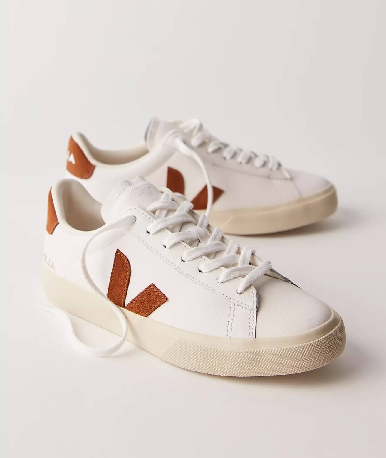 A pair of white low-top sneakers with brown suede "V" logos and accents, beige soles, and white laces—these versatile kicks will have you wanting one in every color. Displayed on a light background.