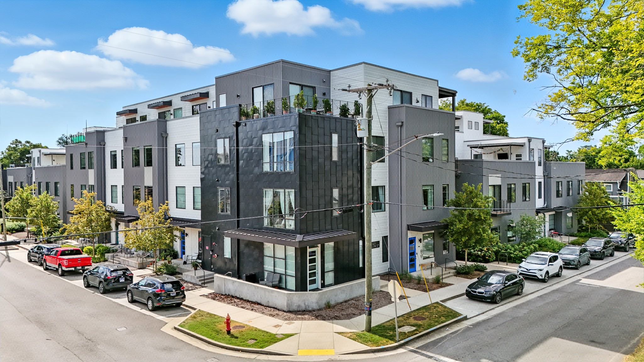 Modern three-story apartment building on the corner of Pillow St in Nashville, with multiple parked cars, trees, and a clear blue sky with a few clouds.