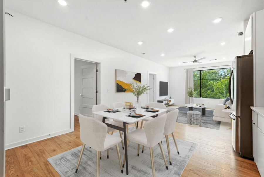 Modern open-plan dining and living area at 1402 Pillow St, Nashville, with white walls, wood flooring, a dining table for six, and a seating area near large windows offering outdoor views.