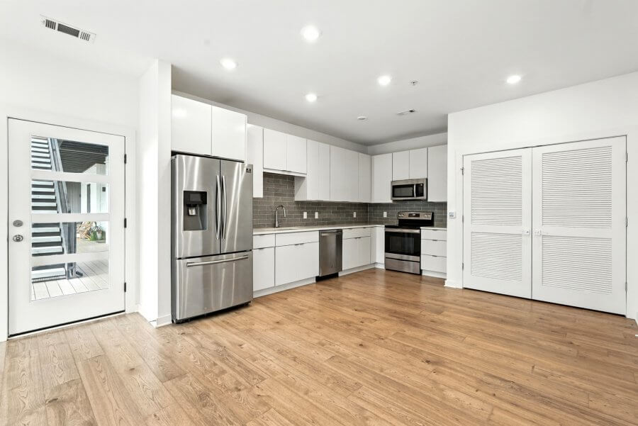Modern Nashville kitchen with stainless steel appliances, white cabinets, gray tile backsplash, and wood flooring. A door and double closet are visible at 1402 Pillow St, with recessed ceiling lights overhead.
