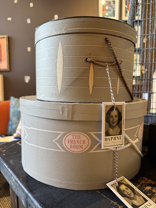 18 Nashville FINDS for Late Summer: Jewelry, Decor & More - 12 Two vintage hat boxes are stacked on a wooden table; both feature decorative labels and attached black-and-white photos of a smiling young girl—a charming Nashville August FINDS discovery.