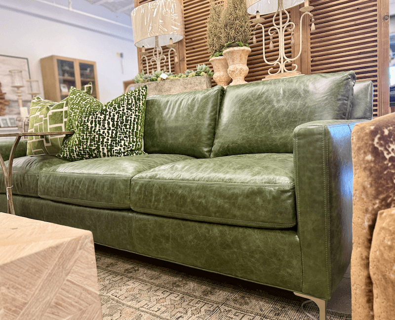 Green Hills green leather sofa with patterned green and white cushions, placed in a living room setting with neutral decor and wooden accents, showcasing Margi’s Furniture design expertise.