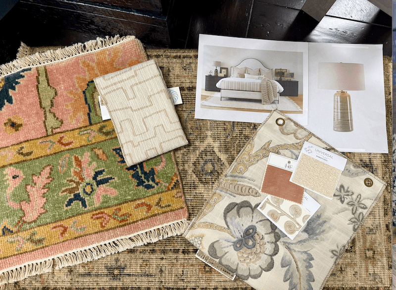 Assorted fabric swatches, rugs, and design samples are laid out on a patterned carpet, alongside printed images of a bedroom and a table lamp—ideal inspiration for interior design projects from Margi’s Furniture.