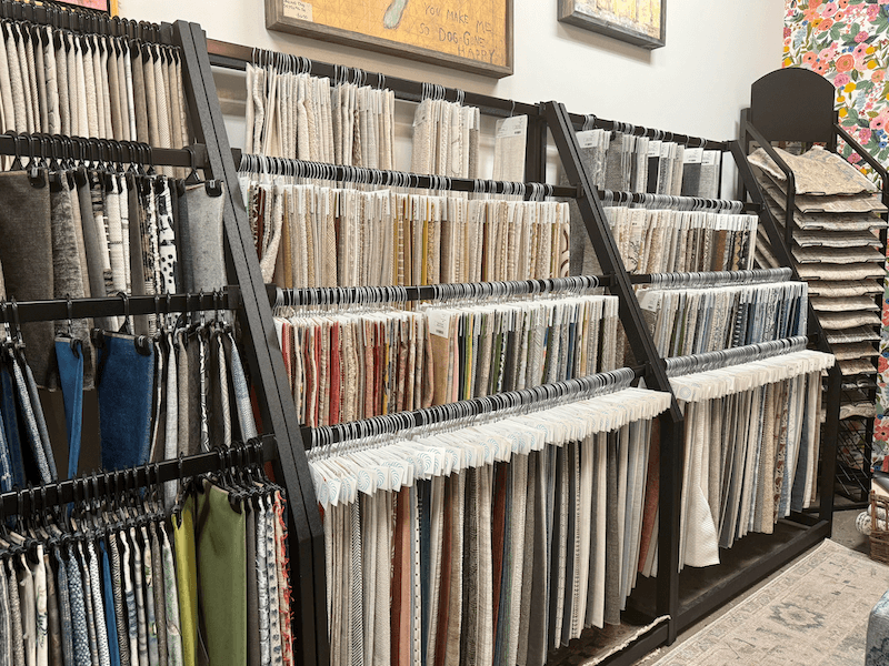 Several racks display numerous fabric samples hanging on hooks, arranged by color and type in Margi’s Furniture showroom, a hub of furniture design inspiration in Green Hills.
