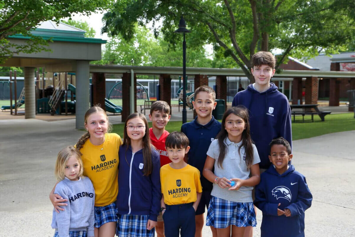 Nashville Private School Open House Dates - 7 A group of children in school uniforms pose and smile outdoors on a Nashville private school campus with playground equipment in the background.