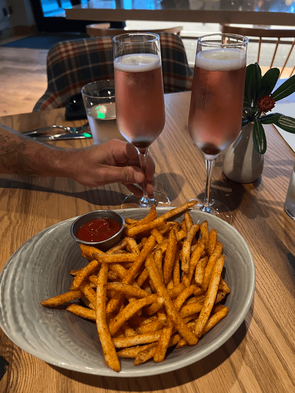 A bowl of seasoned French fries with ketchup and two glasses of sparkling rosé on a wooden table at McLemore Resort; a hand reaches for one glass.