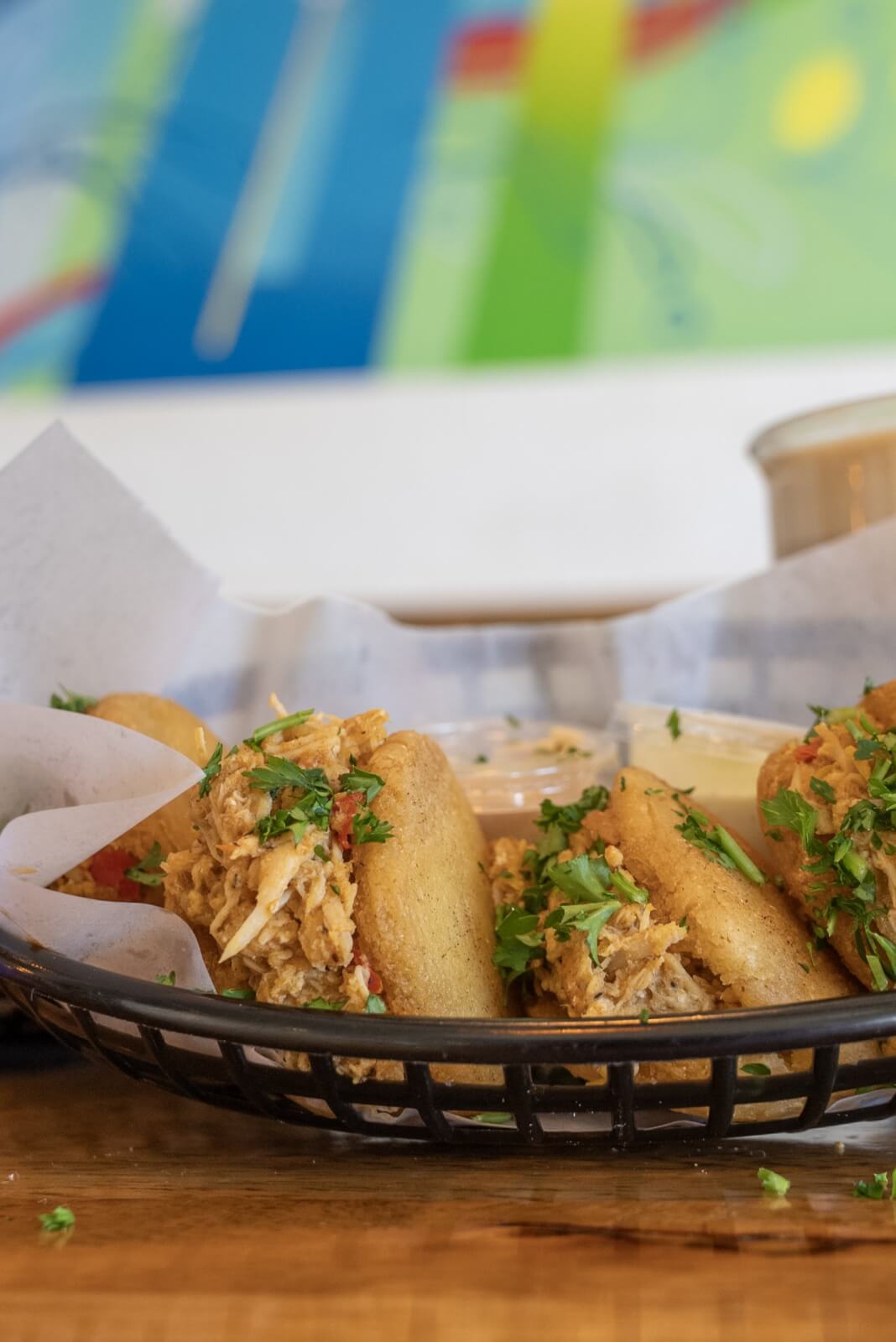 Culinary Road Trip: 4 Tennessee Towns for Food Lovers - 5 A basket of stuffed arepas filled with shredded meat and topped with chopped herbs sits on a wooden table, inviting food lovers on a culinary road trip, with a colorful abstract painting in the background.