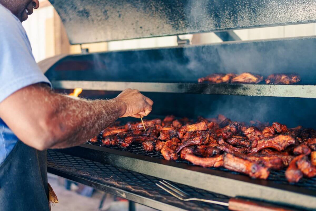 A food lover grills ribs on a large outdoor barbecue smoker, checking the meat as flavorful smoke rises—capturing the essence of a true Tennessee food experience.