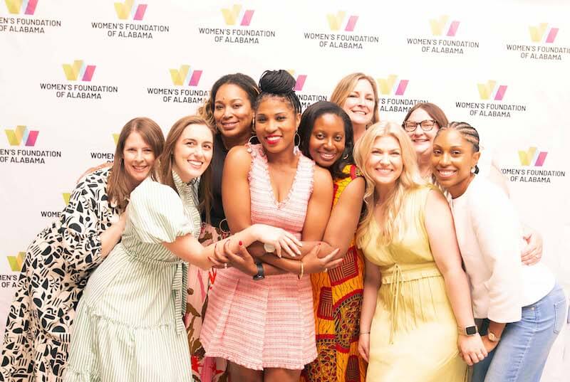 A group of women, including the new CEO, smile and pose together in front of a step-and-repeat banner for the Women's Foundation of Alabama.
