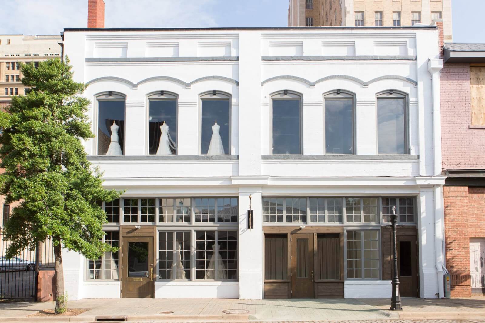 A two-story white brick building with large front windows, displaying mannequins in wedding dresses on the upper floor—home to the Heidi Elnora Atelier.