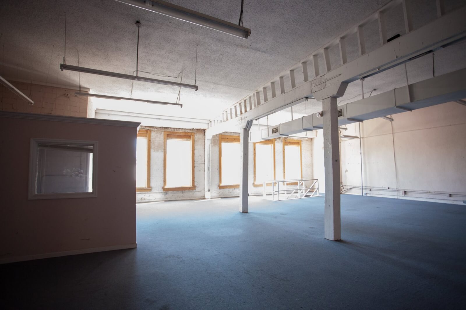 Sunlit industrial Atelier with large windows, exposed beams, modern light fixtures, and a small partitioned office space on the left—a perfect setting for Heidi Elnora’s creative vision. 