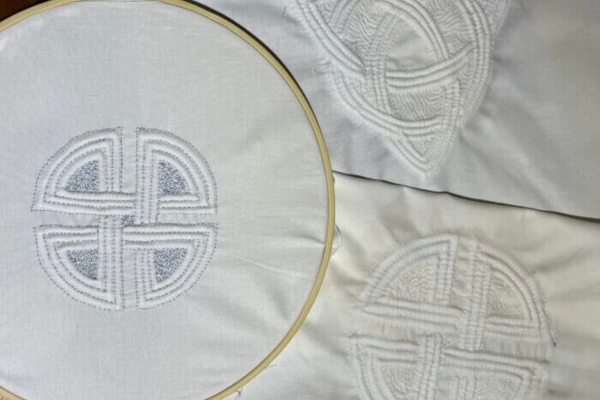 White fabric in an embroidery hoop displays a geometric circular pattern, with two similar stitched designs beside it—perfect inspiration for an Adult ARTlab art workshop exploring Trapunto techniques.