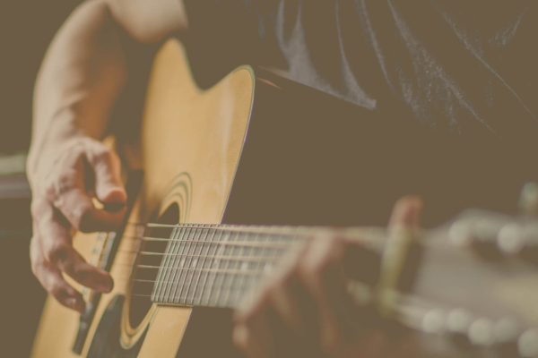 A close-up of a person playing an acoustic guitar at Thistle and Rye, focusing on their hands strumming and fretting the strings during one of the venue’s intimate Writers' Rounds.
