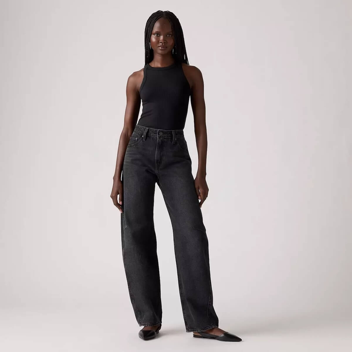 Fall 2025 Fashion: A Stylist's Lookbook of This Season's Trends - 5 A person stands against a plain background wearing a sleeveless black top, high-waisted black jeans, and black flats—an effortlessly chic look inspired by Fall 2025 fashion trends.