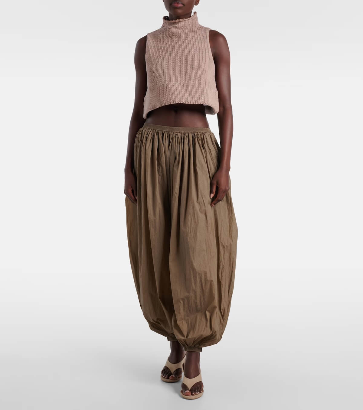 Fall 2025 Fashion: A Stylist's Lookbook of This Season's Trends - 7 A person wearing a sleeveless beige turtleneck crop top, loose brown balloon pants, and open-toe sandals stands against a plain white background, showcasing chic Fall Fashion trends for 2025.