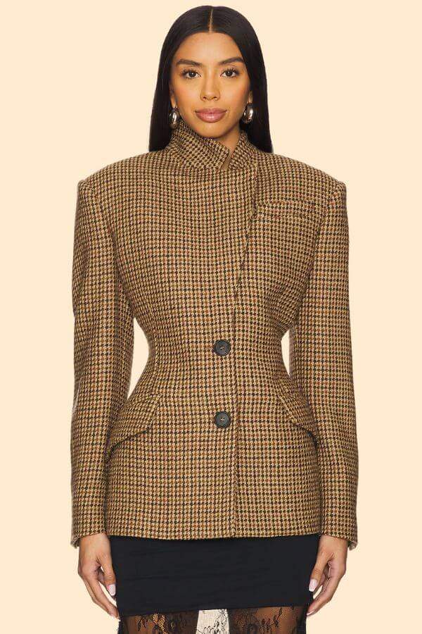 Fall 2025 Fashion: A Stylist's Lookbook of This Season's Trends - 66 A woman wearing a brown houndstooth blazer with prominent shoulders and black buttons, paired with a black skirt, stands against a beige background—an effortless nod to Fall 2025 fashion trends.