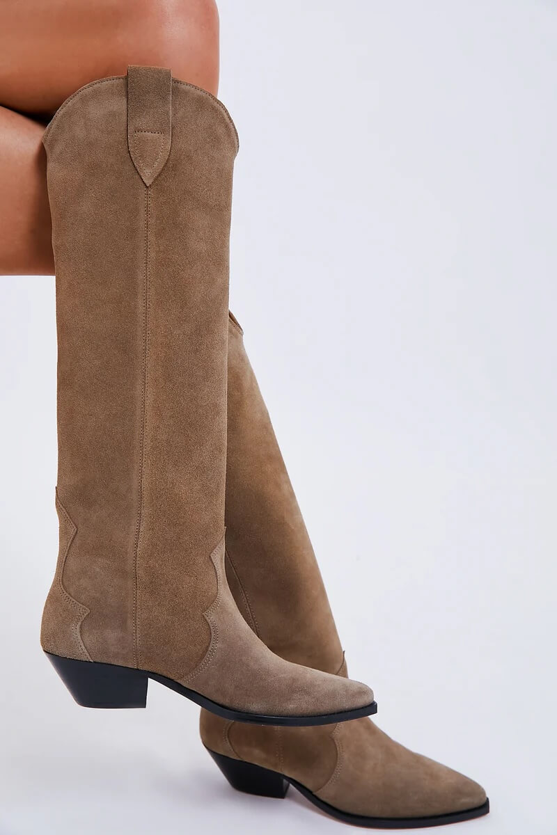 Fall 2025 Fashion: A Stylist's Lookbook of This Season's Trends - 78 A person wears knee-high taupe suede cowboy boots with a pointed toe and low angled heel, capturing the essence of Fall 2025 fashion trends against a plain light background.