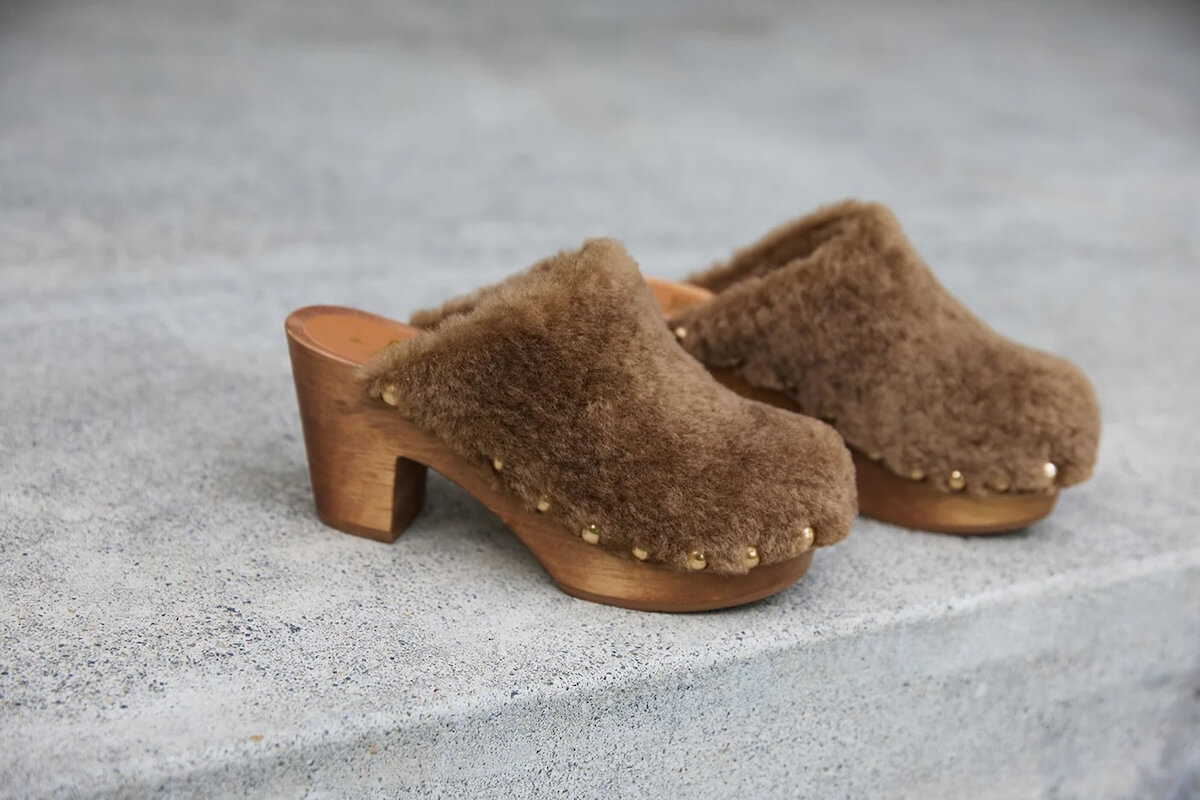 Fall 2025 Fashion: A Stylist's Lookbook of This Season's Trends - 19 A pair of brown, shearling-lined wooden clogs with closed toes and chunky heels, resting on a concrete surface—a stylish nod to fall 2025 fashion trends.