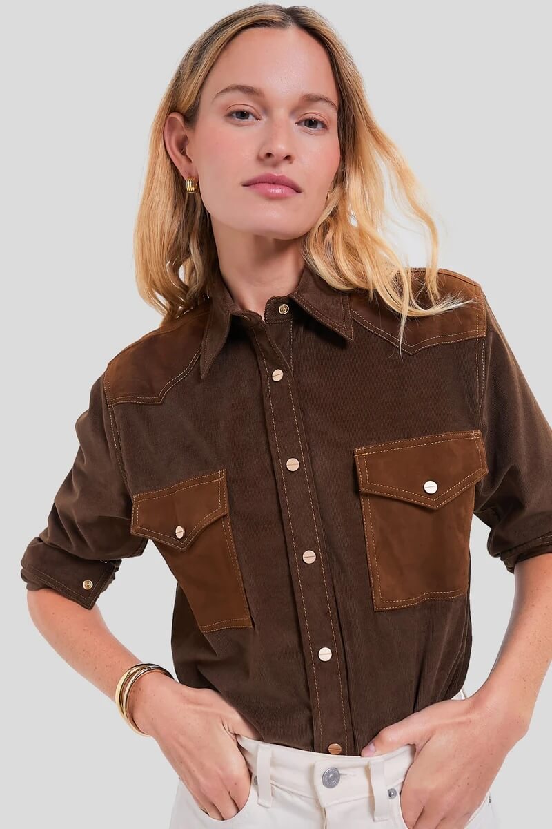 Fall 2025 Fashion: A Stylist's Lookbook of This Season's Trends - 69 Woman wearing a brown button-up shirt with two front pockets, rolled-up sleeves, and white pants, standing against a plain light gray background—perfectly capturing Fall 2025 fashion trends.