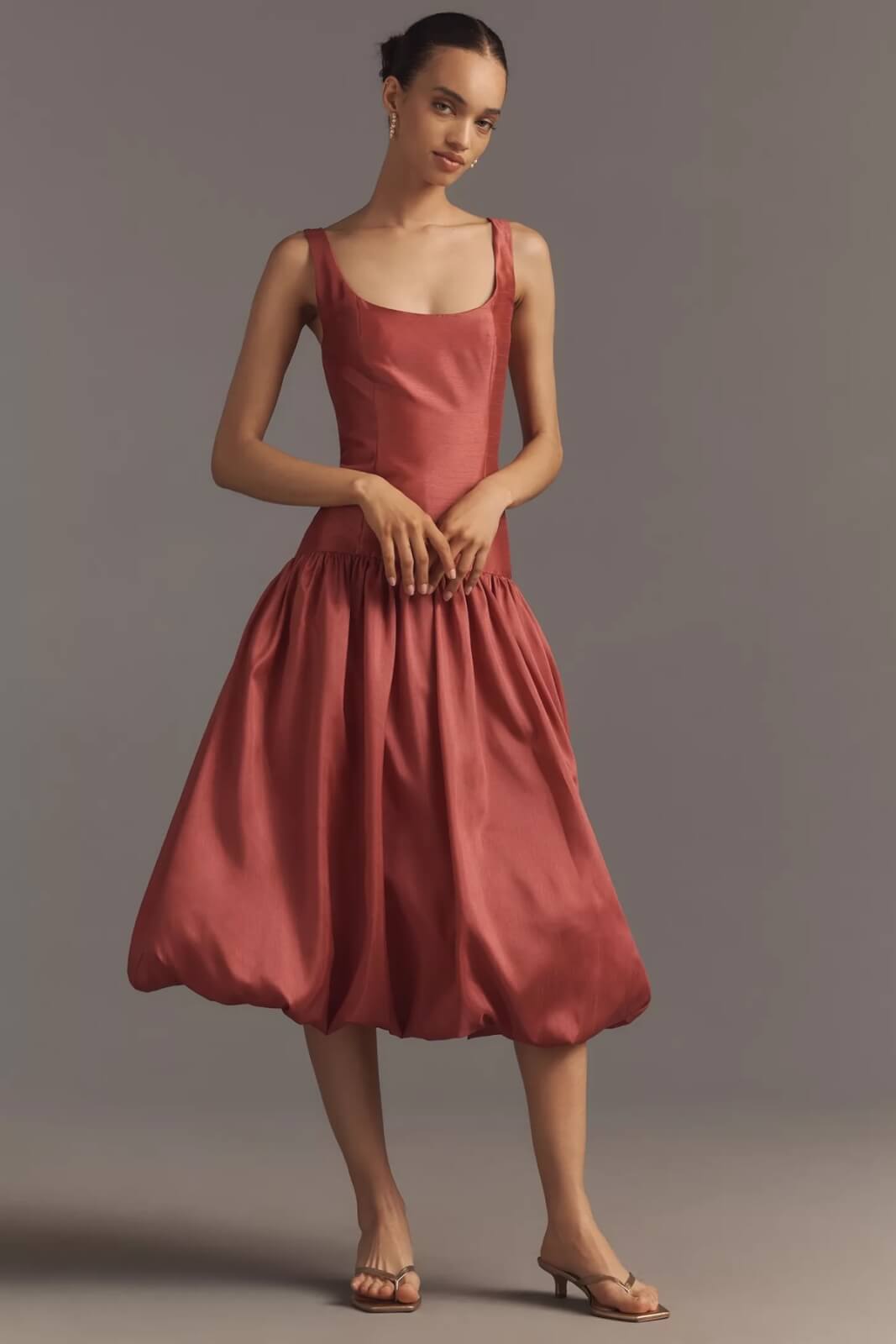 Fall 2025 Fashion: A Stylist's Lookbook of This Season's Trends - 8 A woman stands against a plain background wearing a sleeveless, scoop-neck, rose-colored dress with a fitted bodice and voluminous bubble-style skirt—an elegant nod to fall 2025 fashion—paired with heeled sandals.