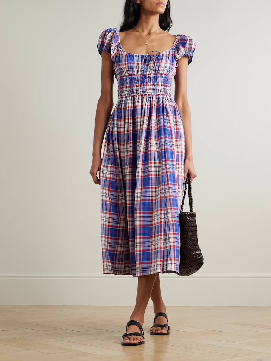 Fall 2025 Fashion: A Stylist's Lookbook of This Season's Trends - 54 A woman wearing a blue, red, and white plaid midi dress with puff sleeves, black sandals, and holding a woven bag stands against a neutral background, showcasing one of the standout Fall Fashion trends for 2025.