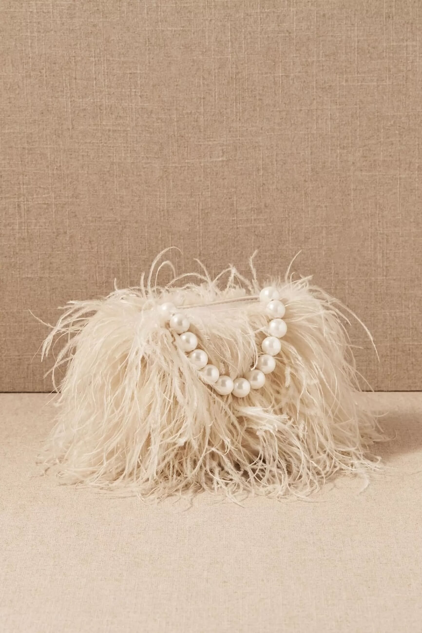 Fall 2025 Fashion: A Stylist's Lookbook of This Season's Trends - 27 A small, cream-colored handbag covered in feathery material with a large pearl-bead handle, set against a neutral fabric background—an elegant accessory inspired by fall 2025 fashion trends.