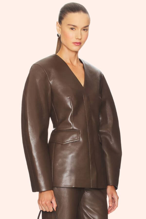Fall 2025 Fashion: A Stylist's Lookbook of This Season's Trends - 13 A woman wearing a structured, dark brown leather jacket and matching pants, holding a small bag, stands against a plain light background—an effortless nod to Fall 2025 fashion trends.