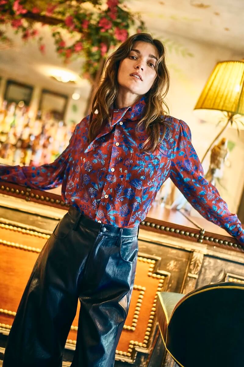 Fall 2025 Fashion: A Stylist's Lookbook of This Season's Trends - 46 A woman stands indoors wearing a red patterned blouse and high-waisted black leather pants, leaning slightly back with her arms extended—a chic nod to Fall 2025 fashion trends.
