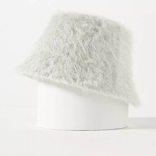 Fall 2025 Fashion: A Stylist's Lookbook of This Season's Trends - 37 A fuzzy, light gray bucket hat—perfect for Fall Fashion 2025—is displayed on a white cylindrical stand against a plain background.