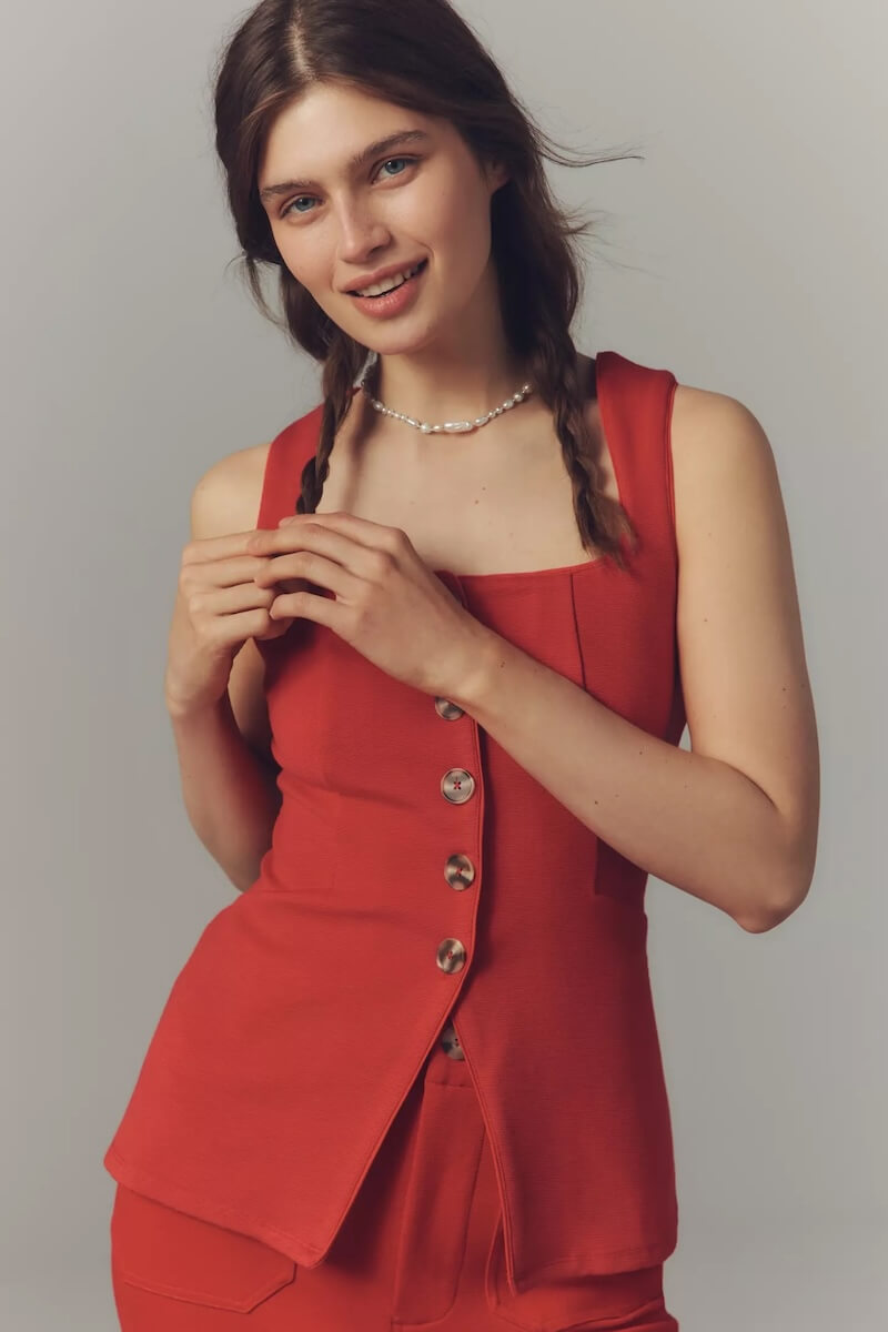 Fall 2025 Fashion: A Stylist's Lookbook of This Season's Trends - 55 Woman with braided hair wearing a sleeveless red buttoned top and matching pants, standing against a plain background and smiling at the camera, showcasing chic fall 2025 fashion.