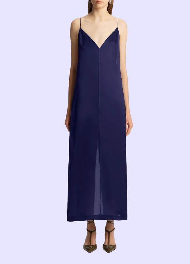 Fall 2025 Fashion: A Stylist's Lookbook of This Season's Trends - 51 A woman wearing a sleeveless, navy blue, V-neck slip dress with thin straps, paired with pointed-toe heels, stands against a light purple background—an elegant nod to Fall 2025 fashion trends.