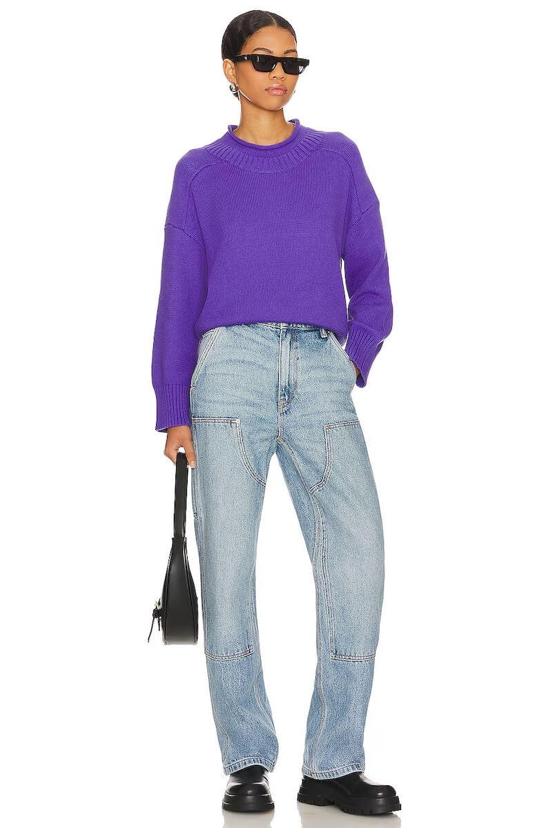 Fall 2025 Fashion: A Stylist's Lookbook of This Season's Trends - 45 A person showcases fall 2025 fashion in a purple sweater, light blue jeans, black shoes, and sunglasses while holding a black handbag against a white background.