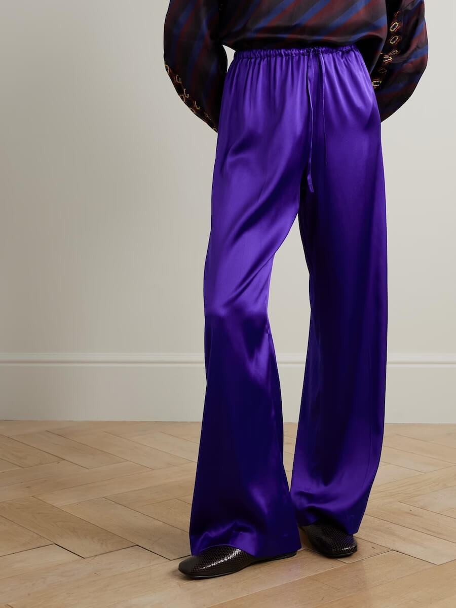 Fall 2025 Fashion: A Stylist's Lookbook of This Season's Trends - 50 Embracing Fall Fashion, this look features loose-fitting, shiny purple satin pants with a drawstring waist, dark shoes, and a striped top—perfectly capturing the bold Fashion Trends of Fall 2025 against a simple wooden floor backdrop.