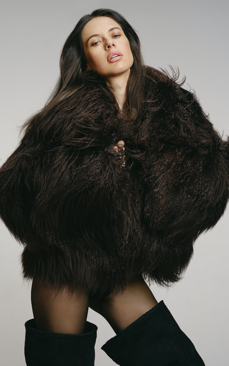Fall 2025 Fashion: A Stylist's Lookbook of This Season's Trends - 28 A woman wearing a large, dark brown fur coat, black stockings, and black boots poses against a plain background, embodying the bold sophistication of Fall 2025 fashion trends.