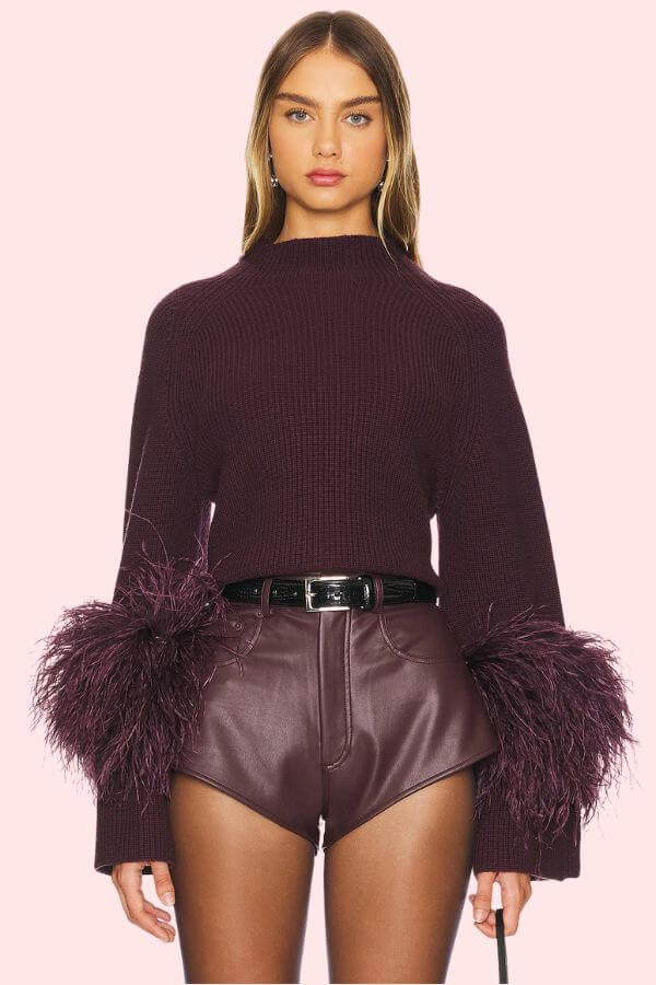 Fall 2025 Fashion: A Stylist's Lookbook of This Season's Trends - 21 Showcasing Fall 2025 fashion trends, this woman pairs a maroon sweater with feathered cuffs and high-waisted leather shorts, finished with a black belt, against a light pink backdrop—perfect for the latest in fall fashion.