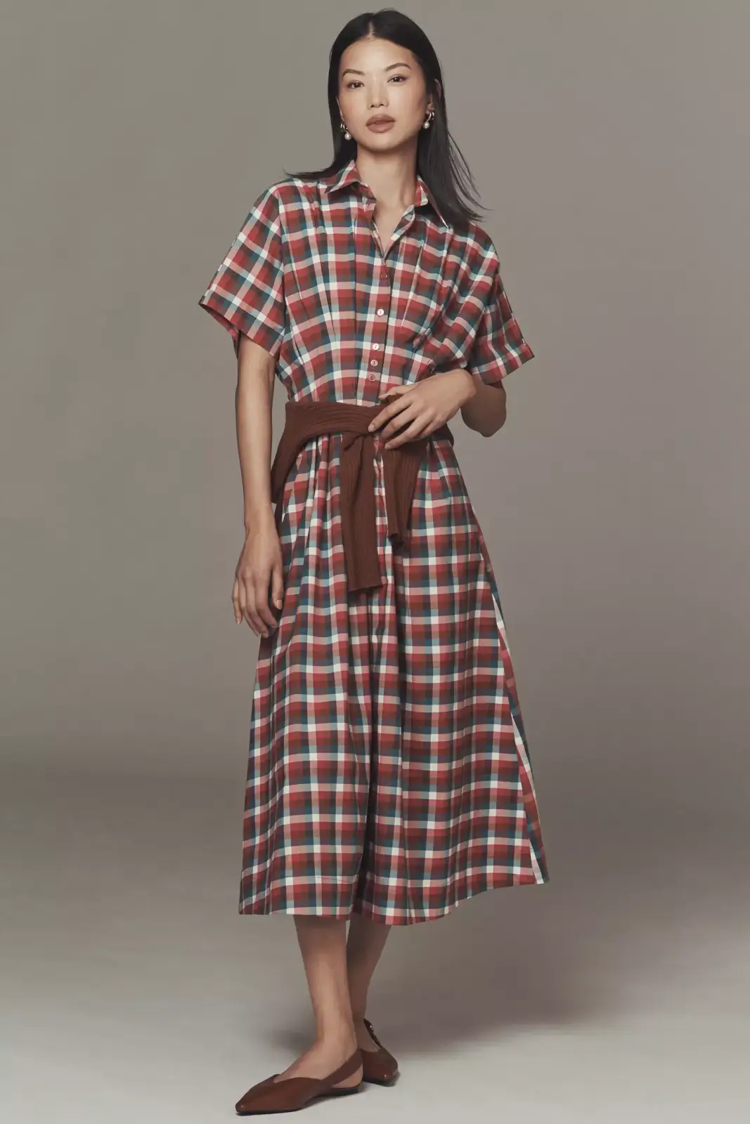 Fall 2025 Fashion: A Stylist's Lookbook of This Season's Trends - 72 A woman wears a red, green, and white plaid button-down midi dress with short sleeves, a brown sweater tied at the waist, and brown flats—capturing effortless fall 2025 fashion.