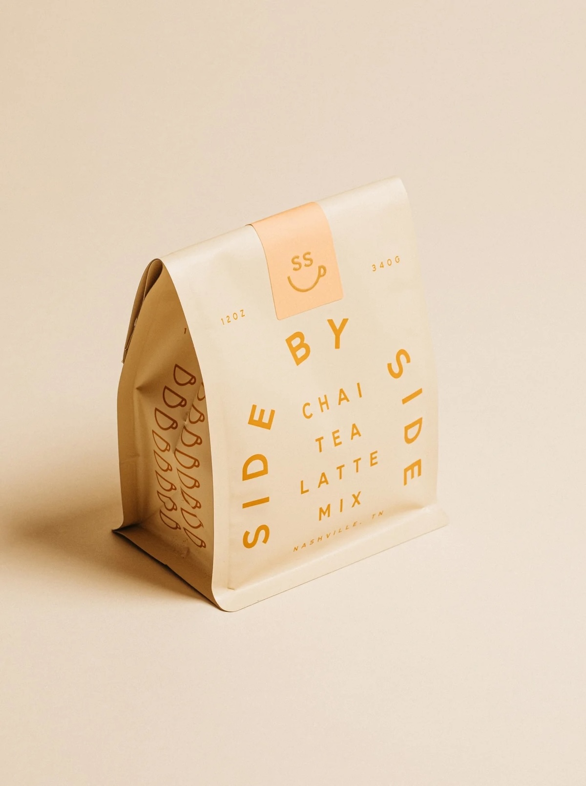 A cream-colored pouch labeled "Side by Side Chai Tea Latte Mix," featured on the SB Hot List, stands upright against a matching beige background. 