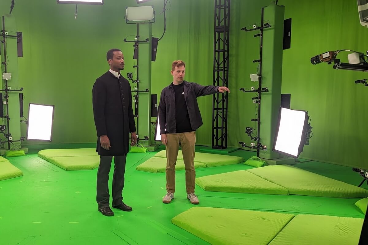 Two men stand on a green screen set with lights and equipment; one man points while the other looks in the same direction, as they prepare to film a scene inspired by the Harlem Hellfighters.